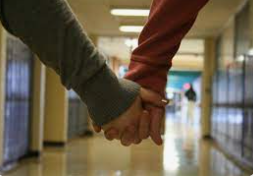 This couple walks through the halls to class  while they are holding hands for everyone to see. 