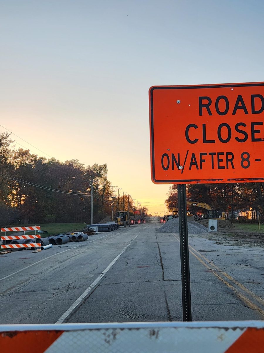 View of sunset looking down construction on Carroll Road from barricades. Shows sewage pipes, drains waiting for installment, and gravel to rebuild the road.